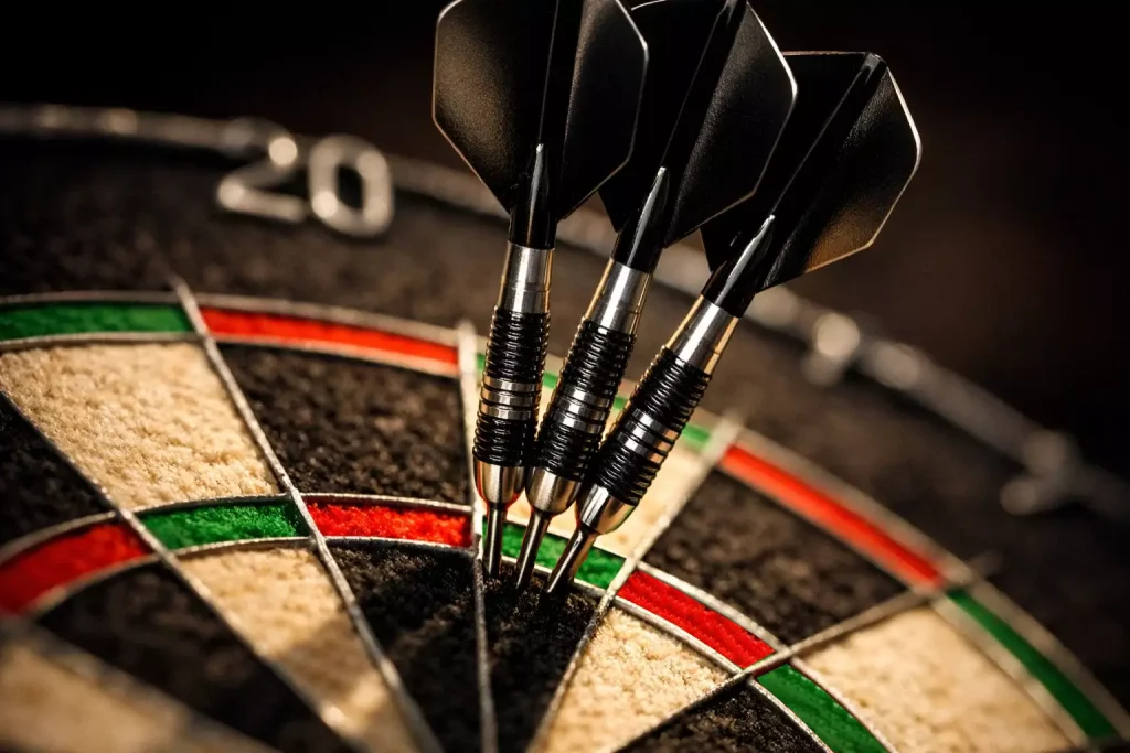 Dartpfeile stecken in der Triple-20 auf einer beleuchteten Dartscheibe in Nahaufnahme